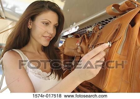 Side profile of a young woman looking at the price tag on a bag in a store View Large Photo Image Stock Photo - Side profile of a young woman looking at the price tag on a bag in a store. Fotosearch