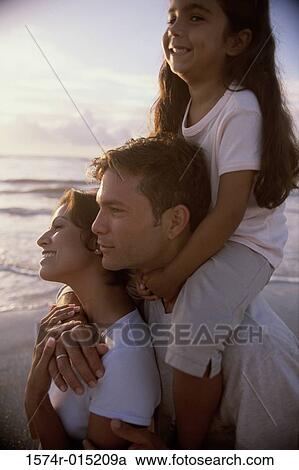 Stock Image - Side profile of parents and their daughter smiling on the beach. Fotosearch
