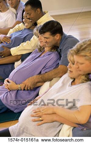 Stock Image - Side profile of pregnant wives and their husbands in a prenatal class. Fotosearch