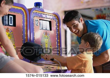 Son playing games with his father standing beside him in an amusement park View Large Photo Image Stock Image - Son playing games with his father standing beside him in an amusement park. Fotosearch