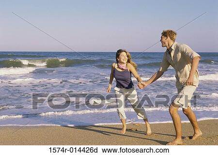 Stock Image - Teenage couple holding hands and running on the beach. Fotosearch