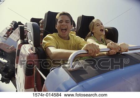 Picture - Teenage couple riding a rollercoaster and screaming. Fotosearch