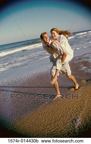 Stock Image - Teenage girl riding piggyback on a teenage boy. Fotosearch