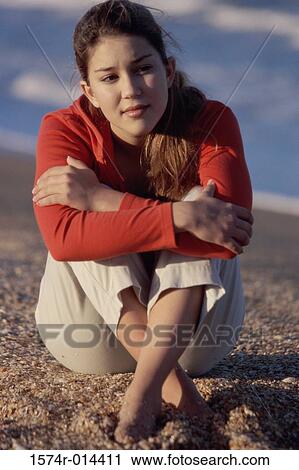 Stock Image - Teenage girl sitting on sand. Fotosearch
