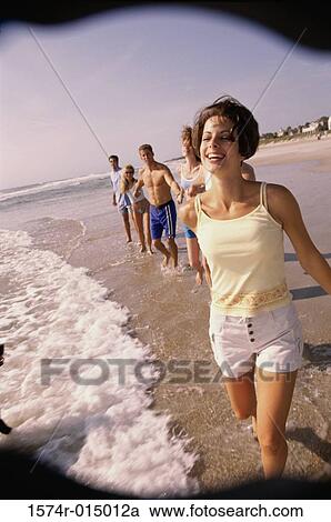 Stock Image - Three young couples holding hands walking on the beach. Fotosearch