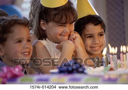 Two boys and a girl smiling in front of a birthday cake at a birthday party View Large Photo Image Picture - Two boys and a girl smiling in front of a birthday cake at a birthday party. Fotosearch