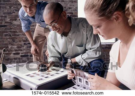 Stock Image - Two businessmen and a businesswoman looking at slides. Fotosearch