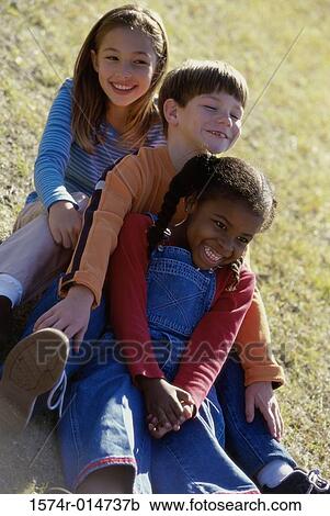 Two girls and a boy sitting on a lawn View Large Photo Image Stock Image - Two girls and a boy sitting on a lawn. Fotosearch