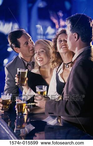 Stock Photo - Two mid adult couples holding glasses of beer in a bar. Fotosearch