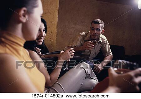 Stock Image - Two young women drinking wine with a young man in a bar. Fotosearch