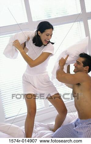 Stock Photo - Young couple having a pillow fight in bed. Fotosearch