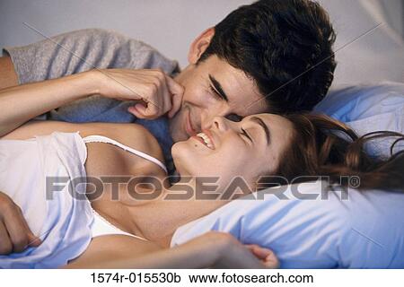 Stock Image - Young couple lying on a bed laughing. Fotosearch