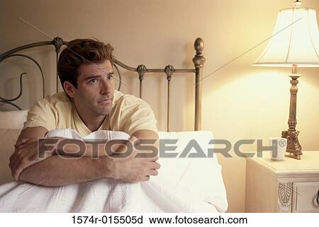 Stock Image - Young man sitting in bed. Fotosearch