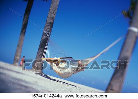 Stock Image - Young man sleeping in a hammock on the beach. Fotosearch