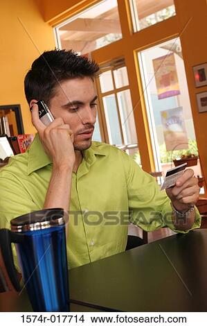 Picture - Young man talking on a mobile phone holding a credit card. Fotosearch