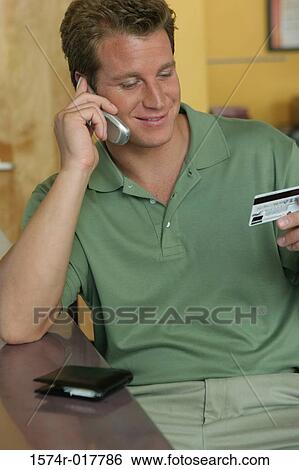 Young man talking on a mobile phone holding a credit card View Large Photo Image Stock Photograph - Young man talking on a mobile phone holding a credit card. Fotosearch