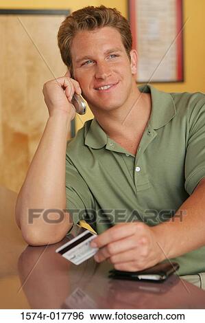 Young man talking on a mobile phone holding a credit card View Large Photo Image Stock Photograph - Young man talking on a mobile phone holding a credit card. Fotosearch