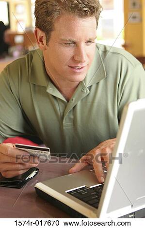 Stock Image - Young man using a laptop holding a credit card. Fotosearch