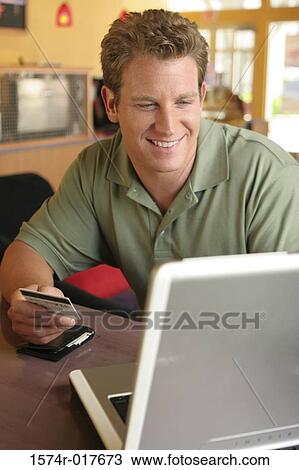 Stock Image - Young man using a laptop holding a credit card. Fotosearch