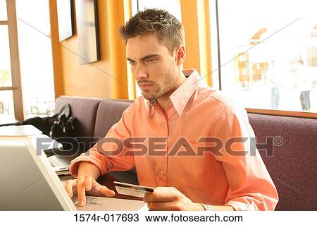 Young man using a laptop holding a credit card View Large Photo Image Stock Image - Young man using a laptop holding a credit card. Fotosearch