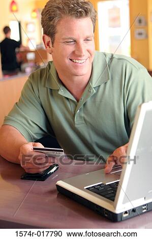 Stock Image - Young man using a laptop holding a credit card. Fotosearch