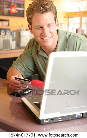 Young man using a laptop holding a credit card View Large Photo Image Stock Image - Young man using a laptop holding a credit card. Fotosearch