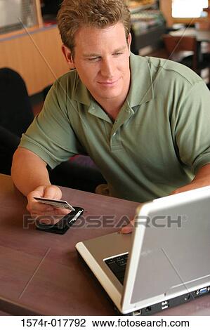 Young man using a laptop holding a credit card View Large Photo Image Stock Image - Young man using a laptop holding a credit card. Fotosearch