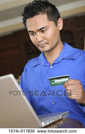 Young man using a laptop holding a credit card View Large Photo Image Stock Image - Young man using a laptop holding a credit card. Fotosearch