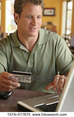 Stock Photography - Young man using a laptop holding a credit card. Fotosearch