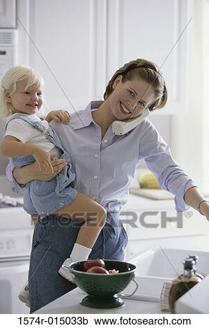 Stock Image - Young woman holding her daughter talking on a telephone. Fotosearch