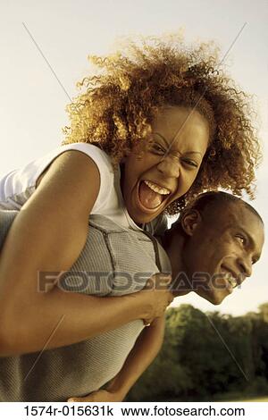 Stock Image - Young woman riding piggyback on a young man. Fotosearch