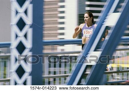 Stock Image - Young woman running on a bridge. Fotosearch