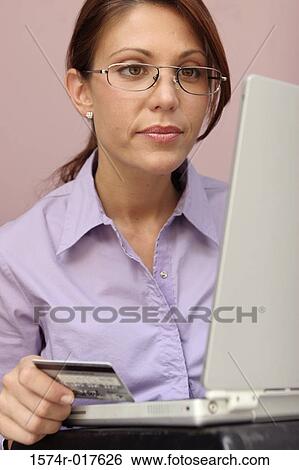 Stock Photograph - Young woman sitting in front of a laptop holding a credit card. Fotosearch