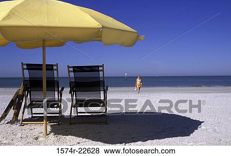 Beach umbrella and two deck chairs on the beach with a young woman walking behind View Large Photo Image Stock Photo - Beach umbrella and two deck chairs on the beach with a young woman walking behind. Fotosearch