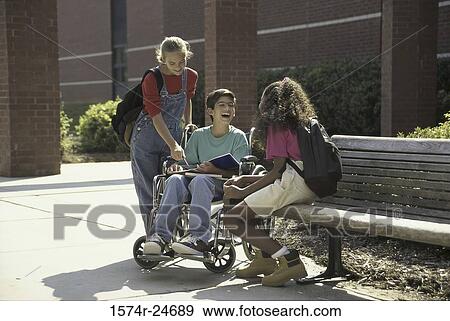 Stock Photo - Boy in a wheelchair talking to two girls outdoors. Fotosearch