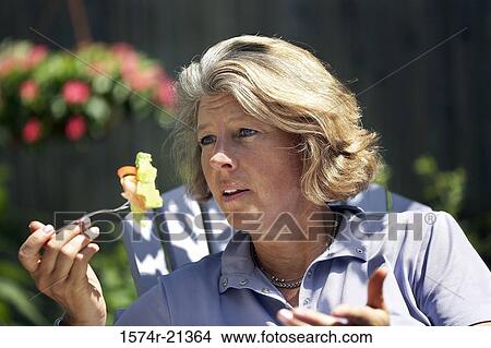 Picture - Close-up of a mature woman eating salad with a fork. Fotosearch
