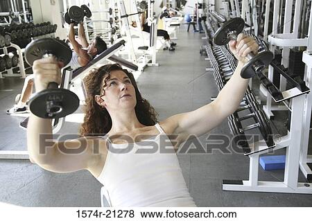 Close-up of a mid adult woman exercising with dumbbells in a gym View Large Photo Image Stock Photo - Close-up of a mid adult woman exercising with dumbbells in a gym. Fotosearch