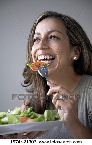 Stock Image - Close-up of a young woman eating salad with a fork. Fotosearch