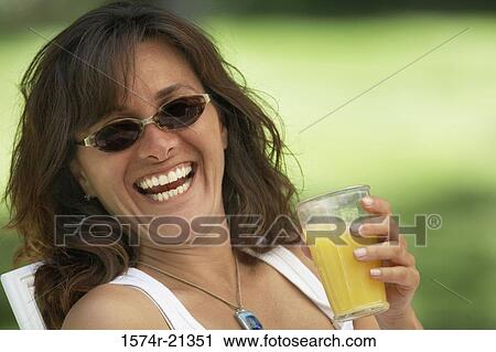 Stock Image - Close-up of a young woman holding a glass of orange juice and laughing. Fotosearch