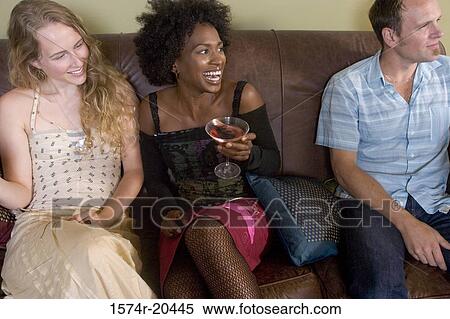 Close-up of two young women and a young man sitting on a couch at a party View Large Photo Image Stock Photography - Close-up of two young women and a young man sitting on a couch at a party. Fotosearch