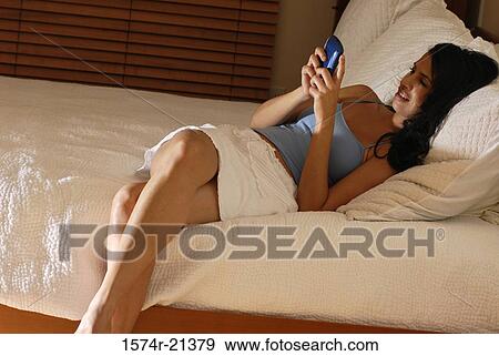 Mid adult woman lying on the bed and using a mobile phone View Large Photo Image Stock Photo - Mid adult woman lying on the bed and using a mobile phone. Fotosearch