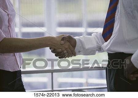 Stock Image - Mid section view of a businessman and a businesswoman shaking hands. Fotosearch
