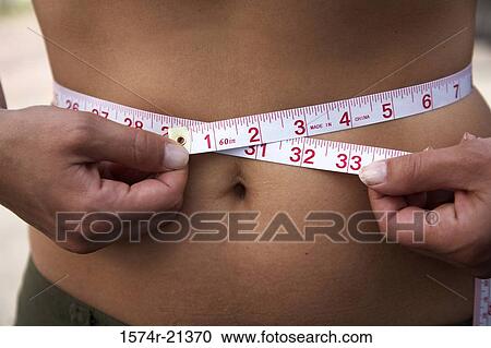 Mid section view of a woman measuring her waist with a tape measure View Large Photo Image Stock Image - Mid section view of a woman measuring her waist with a tape measure. Fotosearch