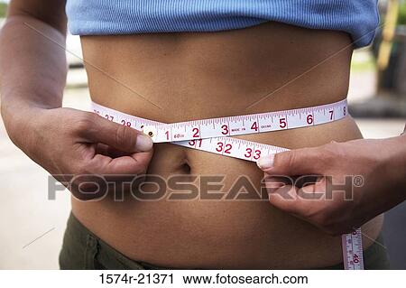 Mid section view of a woman measuring her waist with a tape measure View Large Photo Image Stock Image - Mid section view of a woman measuring her waist with a tape measure. Fotosearch