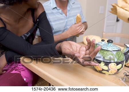 Stock Photograph - Mid section view of a young couple sitting at the dining table. Fotosearch