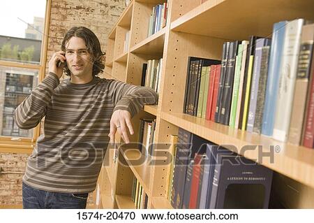 Portrait of a young man leaning against a bookshelf and talking on a mobile phone View Large Photo Image Stock Image - Portrait of a young man leaning against a bookshelf and talking on a mobile phone. Fotosearch
