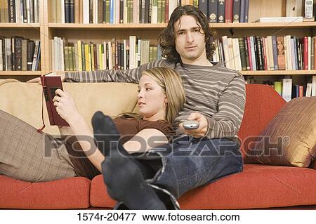 Stock Photo - Portrait of a young man operating a remote control with a young woman relaxing on his lap. Fotosearch