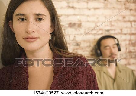 Portrait of a young woman with a young man listening to music in the background View Large Photo Image Stock Photo - Portrait of a young woman with a young man listening to music in the background. Fotosearch