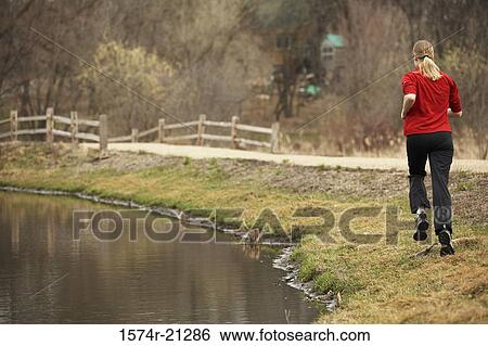 Rear view of a young woman jogging near a pond View Large Photo Image Stock Photograph - Rear view of a young woman jogging near a pond. Fotosearch