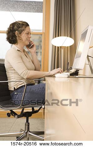 Side profile of a businesswoman talking on a mobile phone while working on a computer View Large Photo Image Stock Photograph - Side profile of a businesswoman talking on a mobile phone while working on a computer. Fotosearch